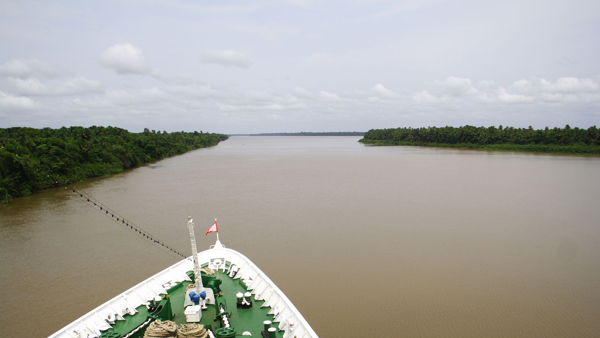 View from the bow of a ship on a wide, forest-lined river